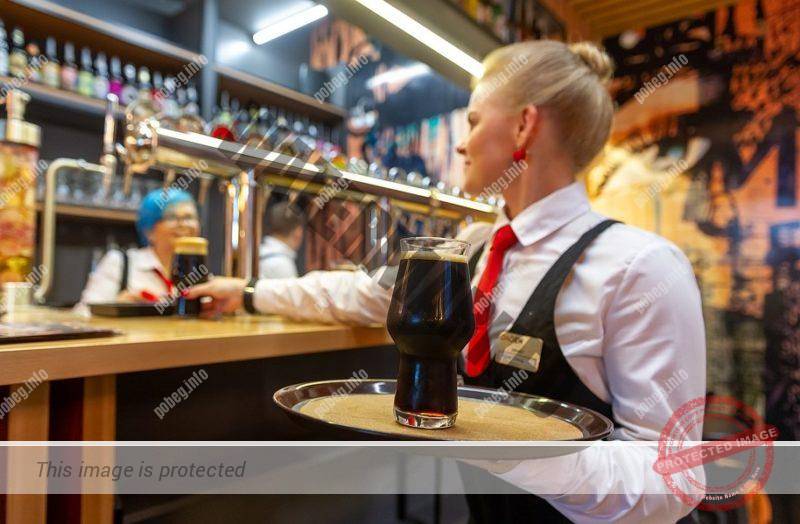 Русская девушка, официантка в баре с бокалом пива